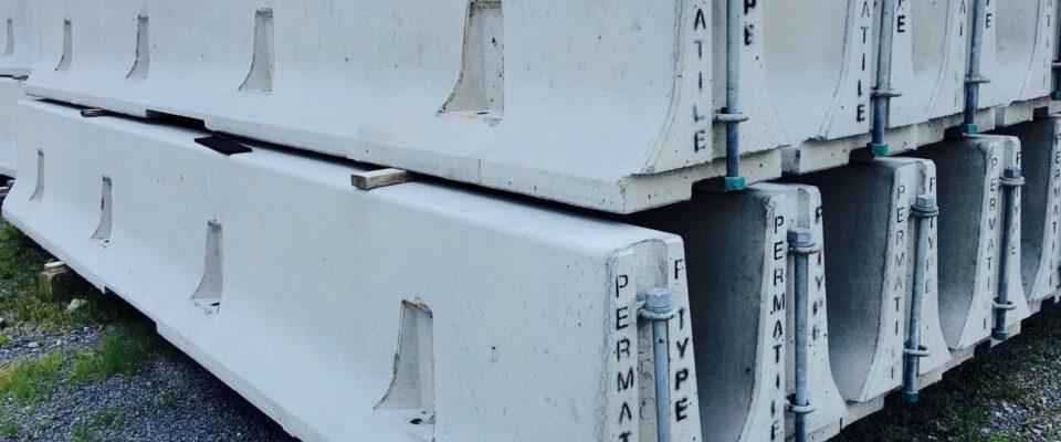 Stacked precast concrete barriers on gravel, labeled Permatile Type, ready for construction projects.