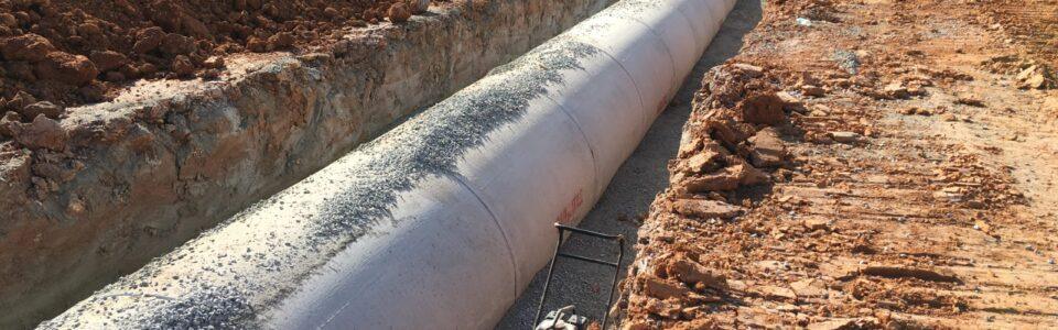 Large precast concrete pipe installed in a trench with surrounding soil and construction equipment visible.