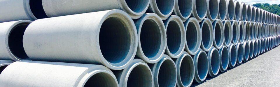 Stacks of large precast concrete pipes under a clear sky at a construction site, ready for infrastructure projects.
