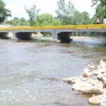 Precast concrete bridge over a rocky river, with trees and a few people on the bridge.