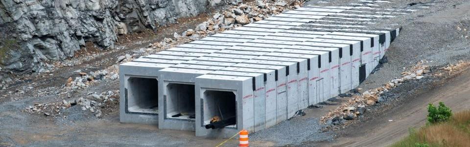 Precast concrete culverts in a line at a construction site, surrounded by gravel and rock, showcasing durable infrastructure.