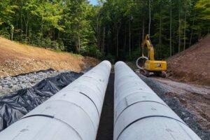 Two parallel 120-inch reinforced concrete pipes installed in trench with excavator on site