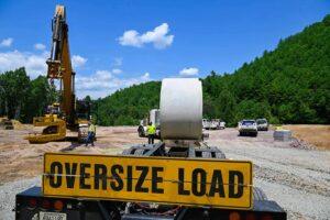 120-inch concrete pipe on flatbed trailer with oversize load sign and workers on site