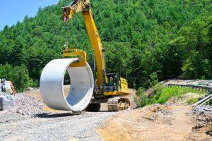 Excavator lifting large reinforced concrete pipe section during Route 321 installation