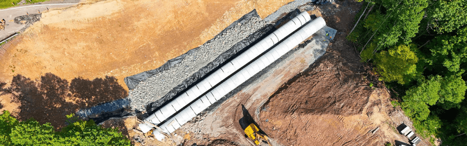 Aerial view of precast concrete pipes installed at a construction site with surrounding dirt and machinery.